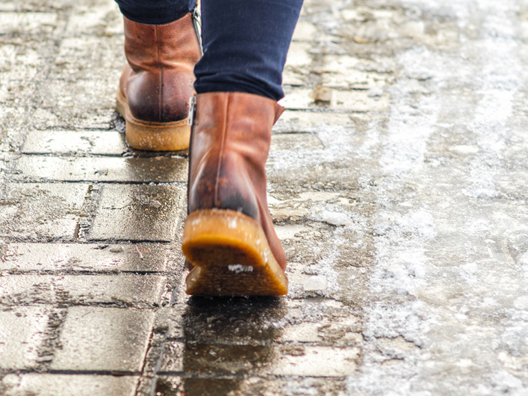 image of a person's feet in boots walking on an icy sidewalk